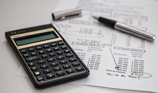 Calculadora, caneta e tampa sobre uma mesa com um relatório contendo números simbolizando a gestão financeira de um posto.