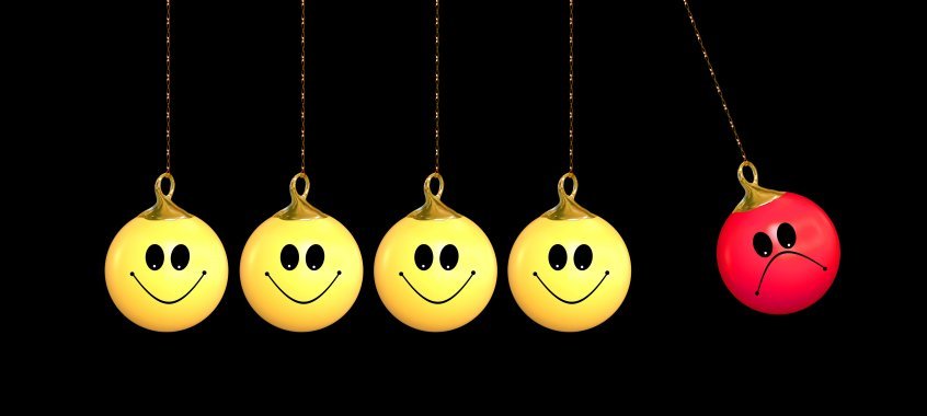 A ilustração mostra cinco bolas presas em correntes com smiles: quatro amarelas felizes e uma vermelha triste. As quatro amarelas estão paradas juntas, enquanto a vermelha se move sozinha, mostrando como a motivação no trabalho forma equipes unidas.