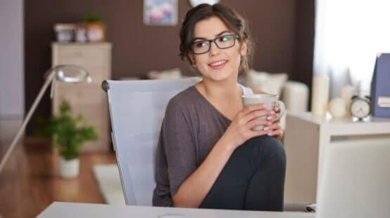 Imagem mostra mulher jovem sozinha com copo de café na mão em sua mesa, como se perguntasse se posso abrir escritório de contabilidade sozinha