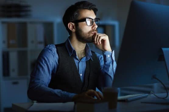 Imagem mostra investidor com rosto pensativo olhando para o computador, para simbolizar como declarar criptomoedas no imposto de renda